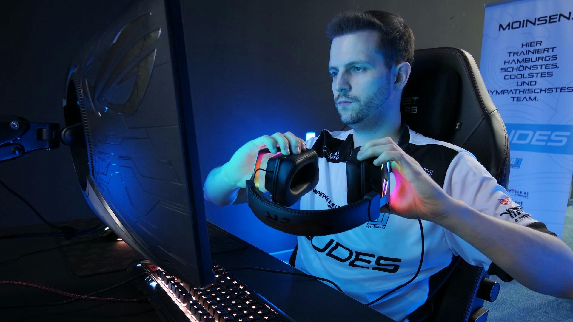 Ein Esport Spieler sitzt vor einem Gaming PC mit beleuchteter LED Gaming Tastatur und setzt sich ein LED Gaming Headset auf