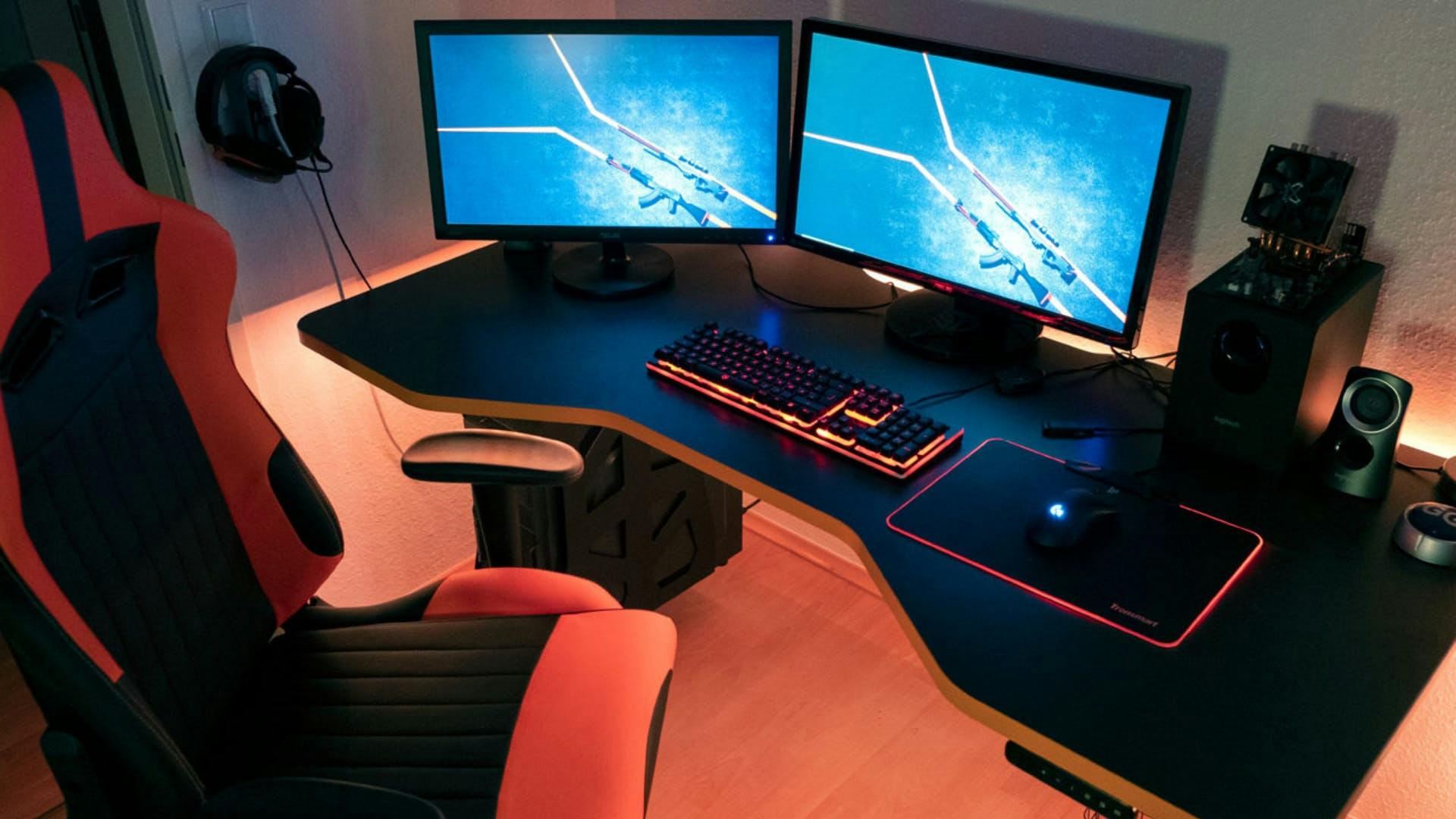 An einem Gaming Tisch von LeetDesk steht ein Gaming Stuhl, auf dem Tisch stehen zwei Gaming Monitore, eine LED Gaming Tastatur, ein Gaming PC und eine Gaming Maus auf einem Gaming Mauspad