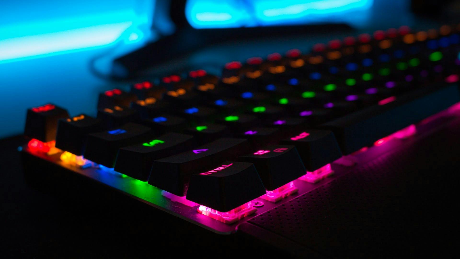Eine in regenbogenfarben erleuchtete LED Gaming Tastatur in einem dunklen Setup aus der Seitenansicht 