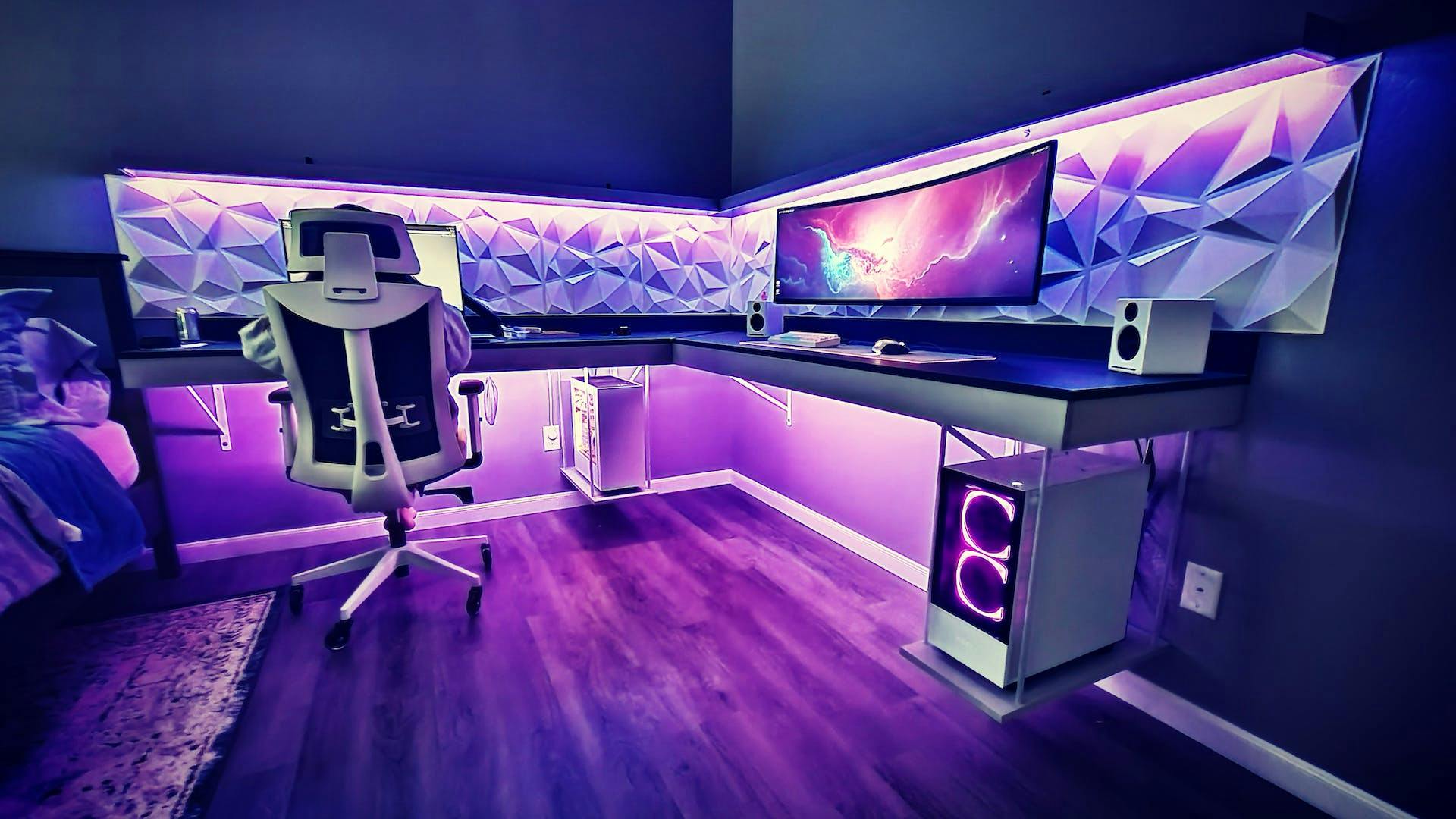 In einem mit lila LED beleuchteten Gaming Zimmer mit Gaming Setup in weiß steht ein großer Gaming Tisch mit einer Ecke, auf dem ein ultrawide Monitor steht 