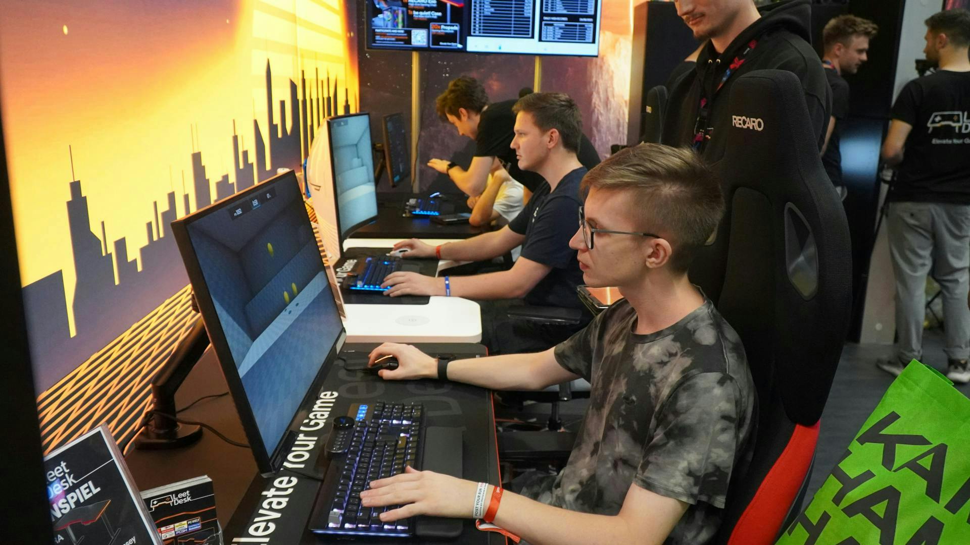 Gamescom visitors sit on LeetDesks and are taking part in the Aim Challenge  