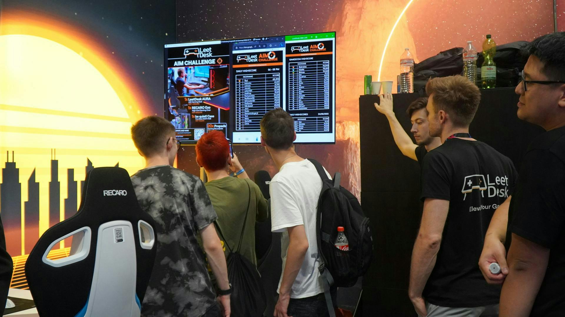 Des visiteurs de la Gamescom observent avec curiosité le tableau des scores du défi de précision au stand LeetDesk de la Gamescom.
