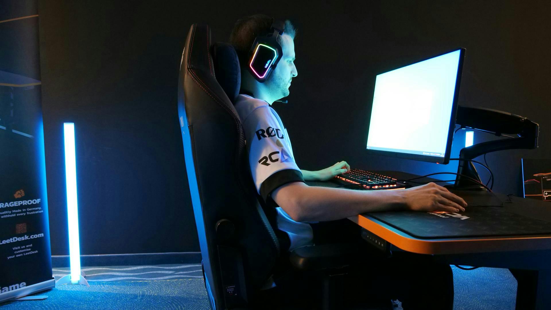 Eine Person mit LED Headset sitzt gerade, hell erleuchtet durch einen Bildschirm am LeetDesk Monitorarm, an einem Gaming Tisch von LeetDesk 