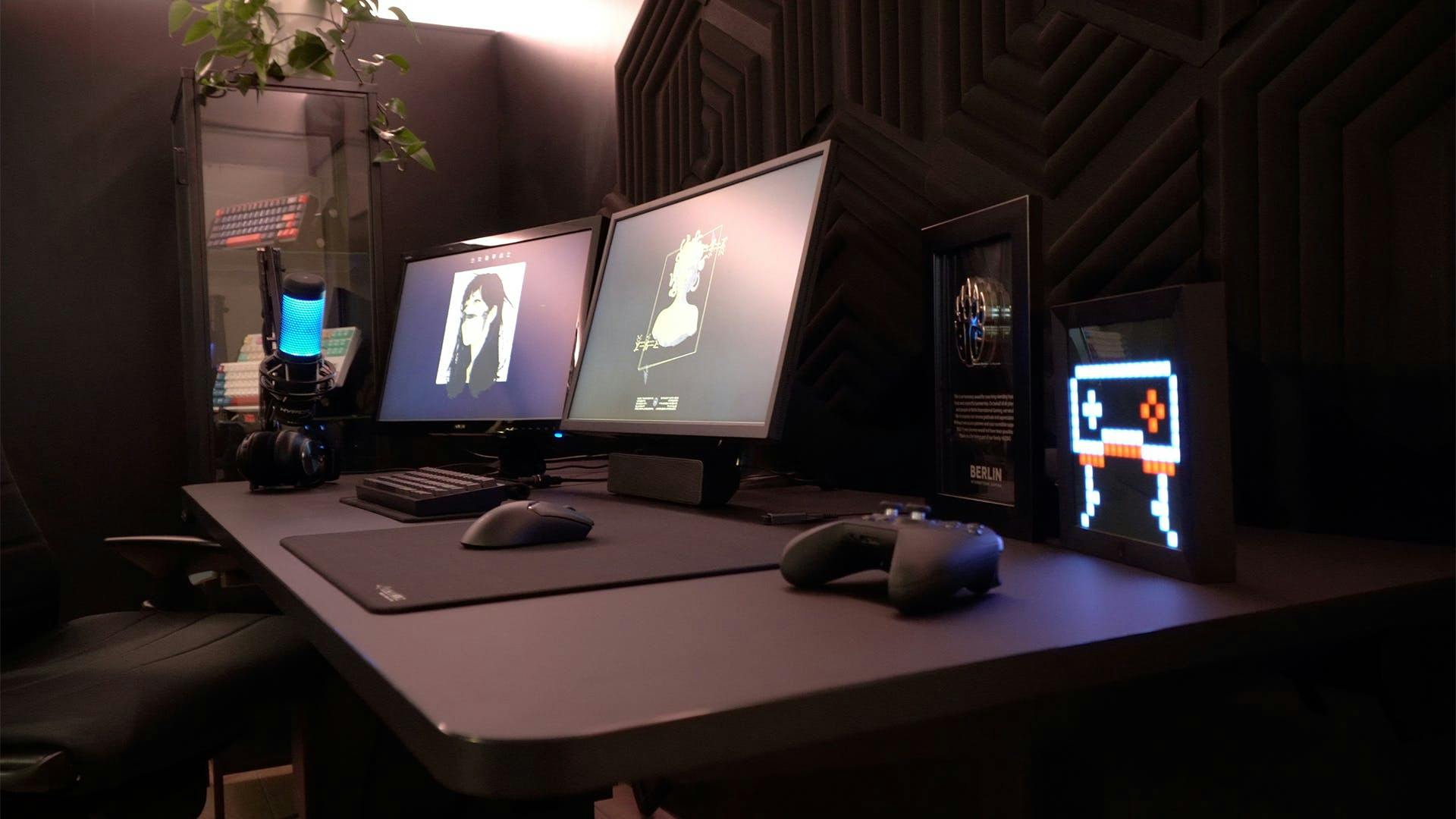 A gaming setup with black elements such as a gaming table, two gaming monitors, a microphone and decoration with LED effects.