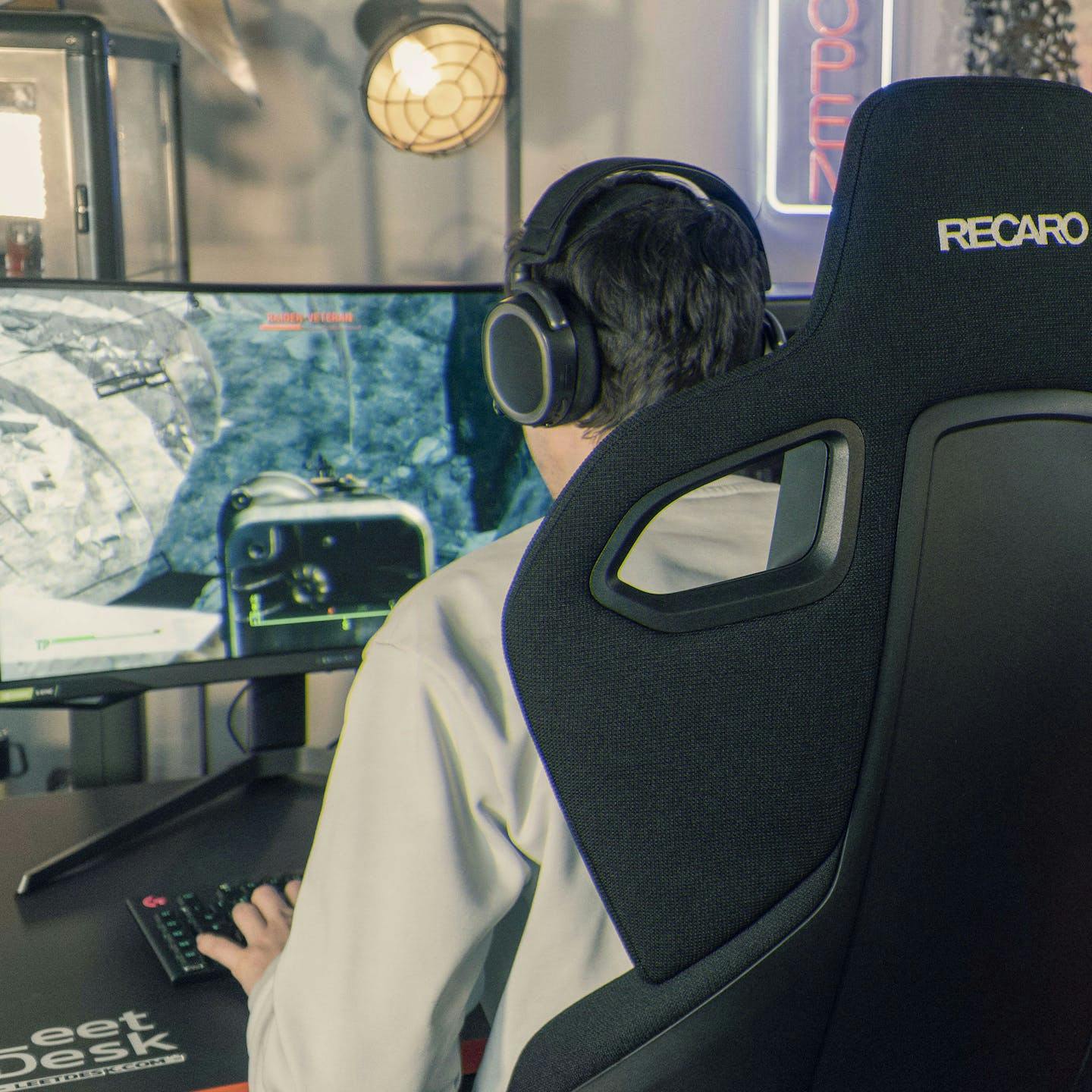 Gamer sits on a Recaro gaming chair at a LeetDesk gaming table, engrossed in a game.