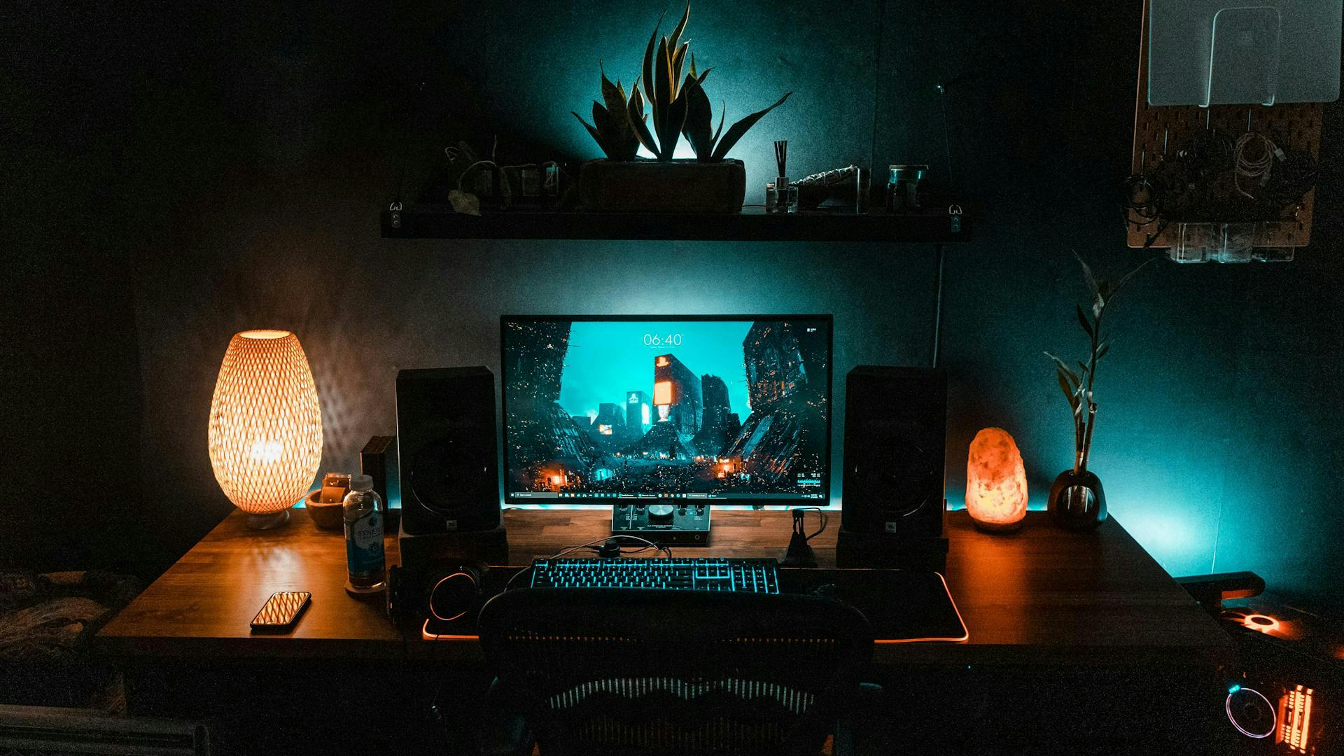 A dark room is coherently illuminated by turquoise and orange light elements in the gaming setup