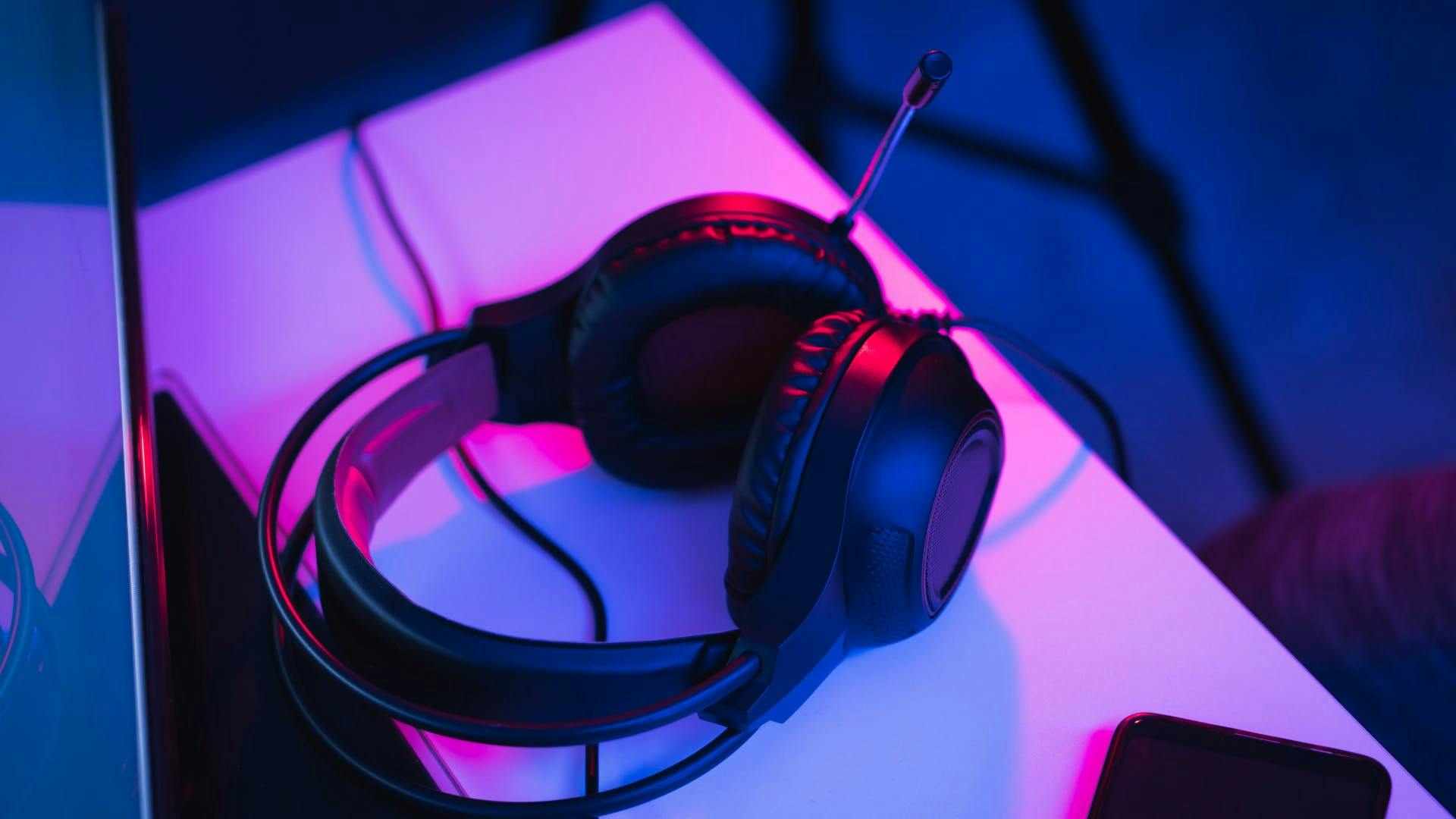 A gaming headset on a gaming desk in a glowing pink LED gaming setup