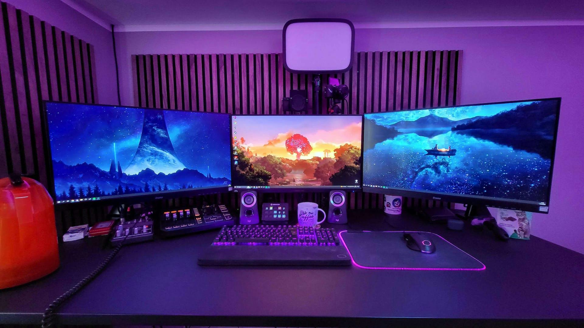 A gaming setup with purple LED lighting, LeetDesk, three monitors and large mouse pad