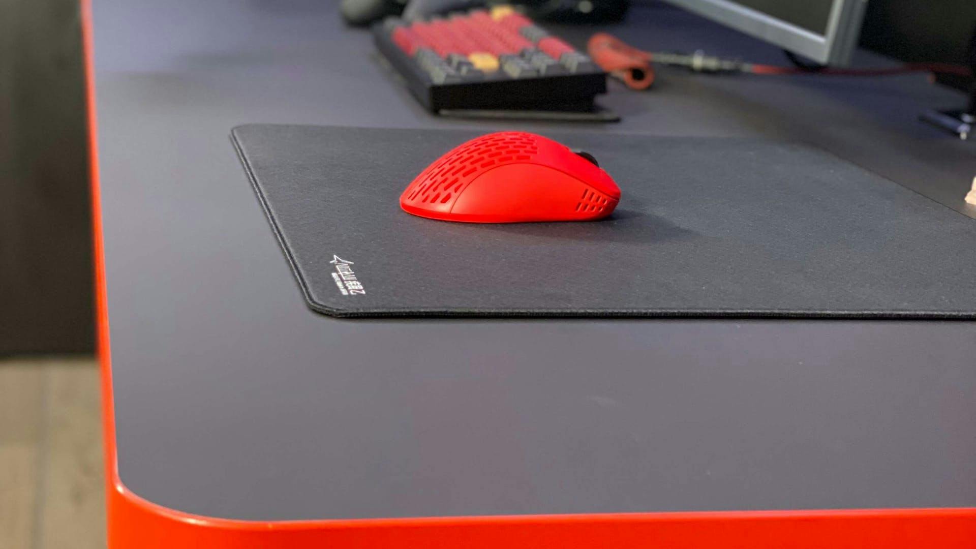 Eine kleine, rote Gaming Maus mit liegt auf einem Gaming Mauspad von LeetDesk auf einem Gaming Tisch von LeetDesk