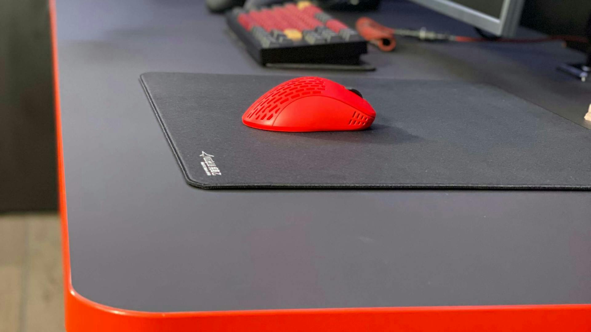 A small red gaming mouse with lies on a gaming mouse pad from LeetDesk on a gaming table from LeetDesk